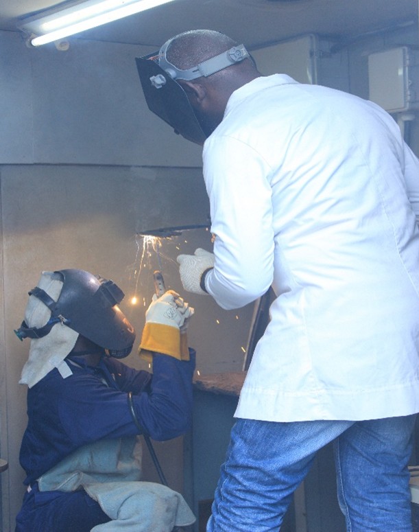 Instructor guiding a seated trainee through a welding exercise