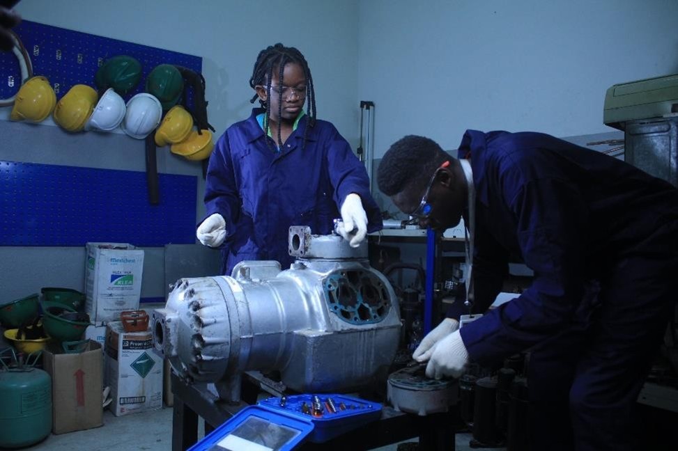 Two BVC trainees dismantling an industrial compressor on a workbench
