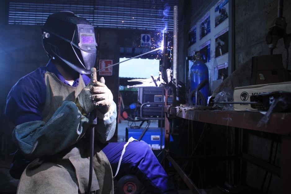 BVC trainee in a welding helmet and leather apron striking an arc on a steel section
