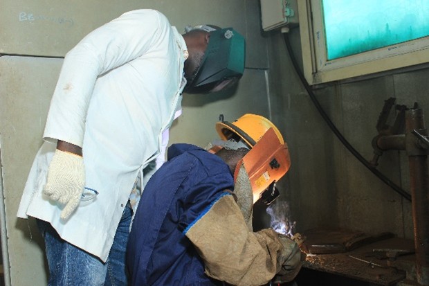 Instructor supervising a trainee welding inside a booth